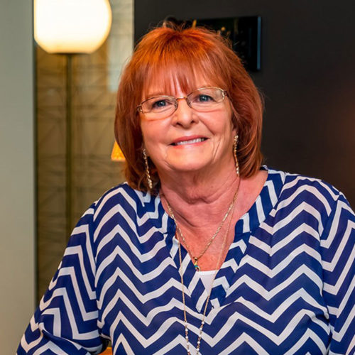 Joanne- Woman with short red hair smiling wearing glasses and a chevron print blouse