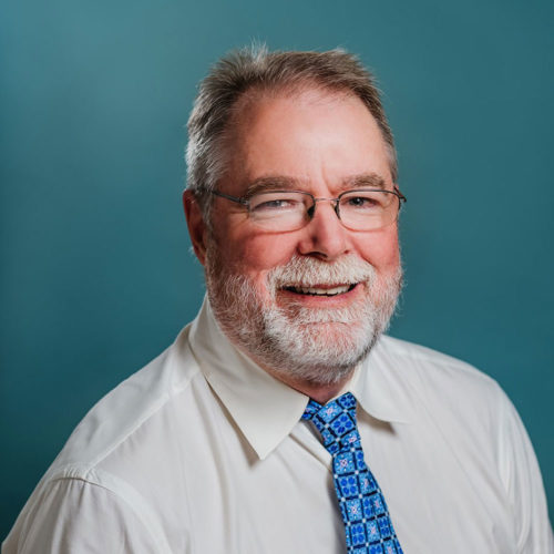 Dr. Morrison Older man with white beard wearing a white button down shirt and blue tie