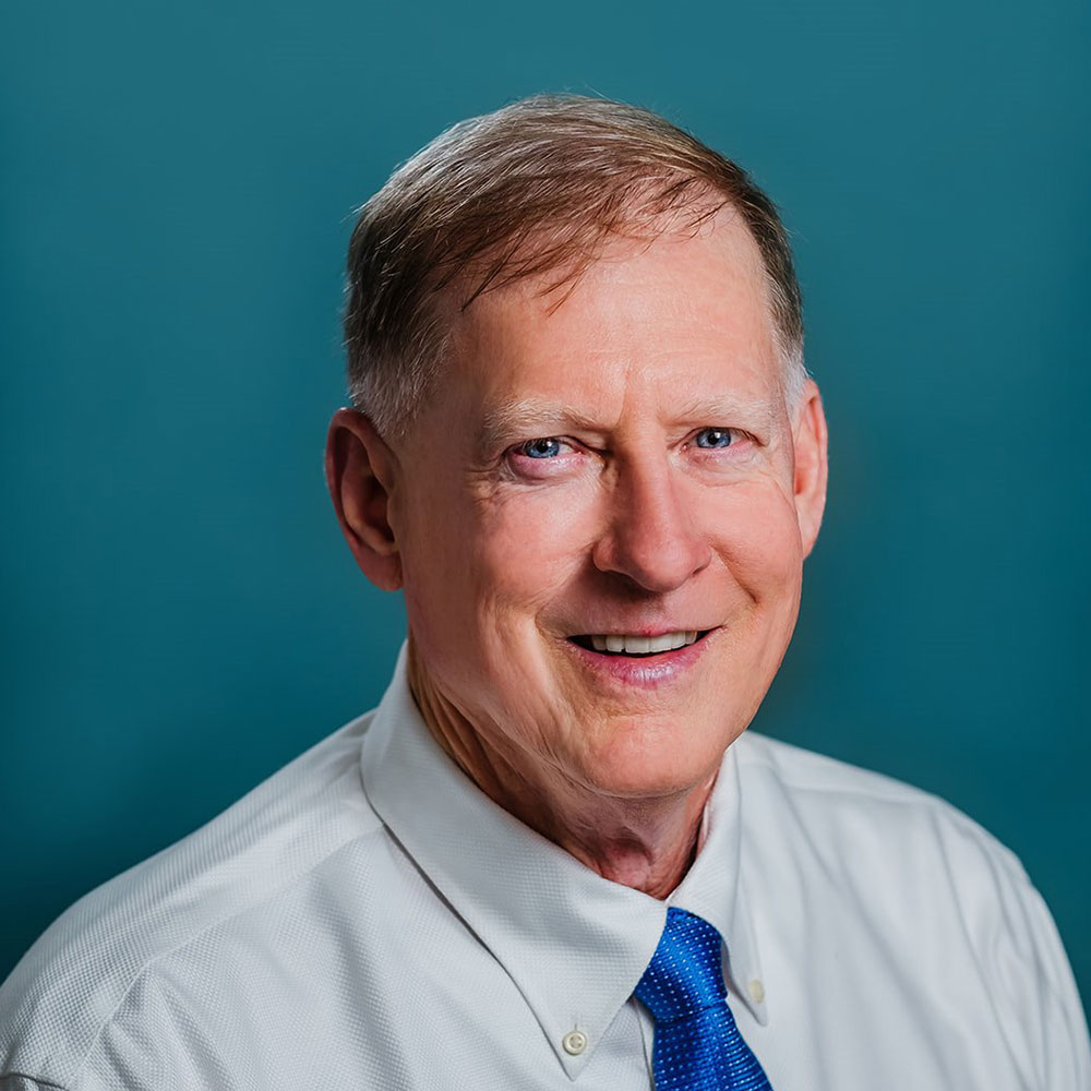 Dr. Jacobs- older man smiling wearing a white button down and royal blue tie